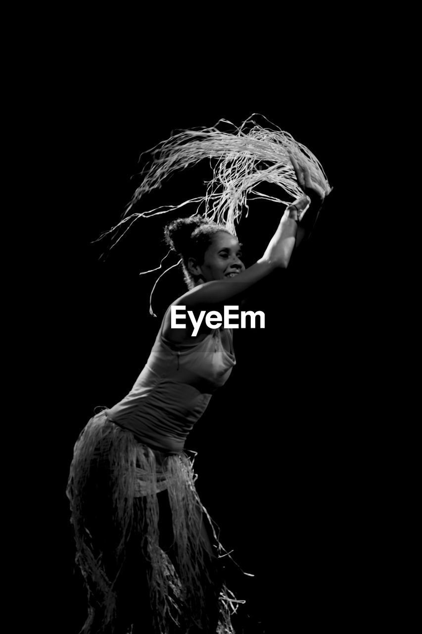 Contemporary dancer dancing in theater with black background and straw accessory. 