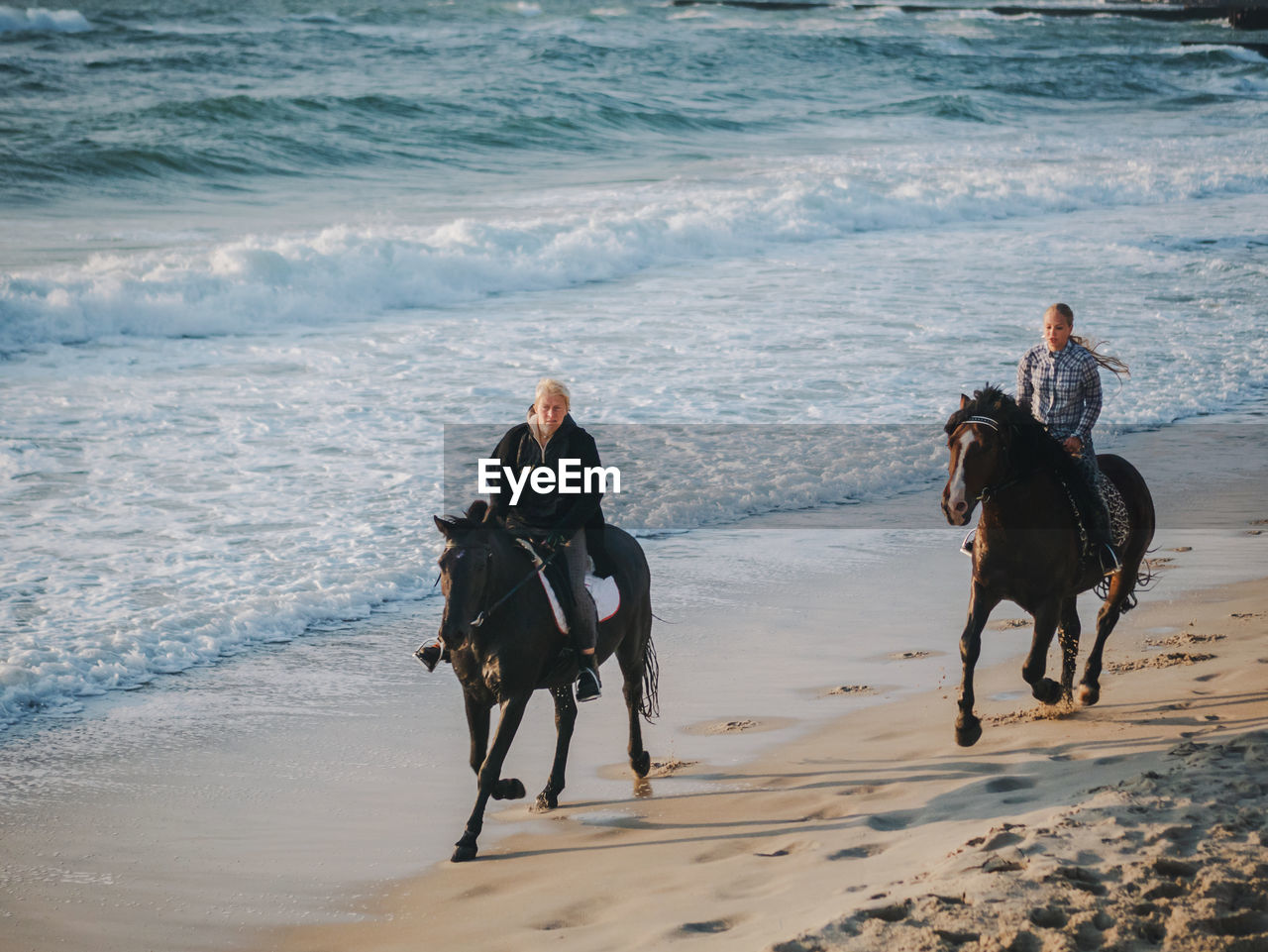 Friends horseback riding on shore at beach