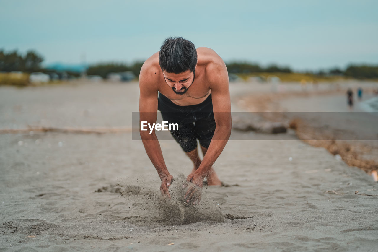 Full length of shirtless man on beach exercising