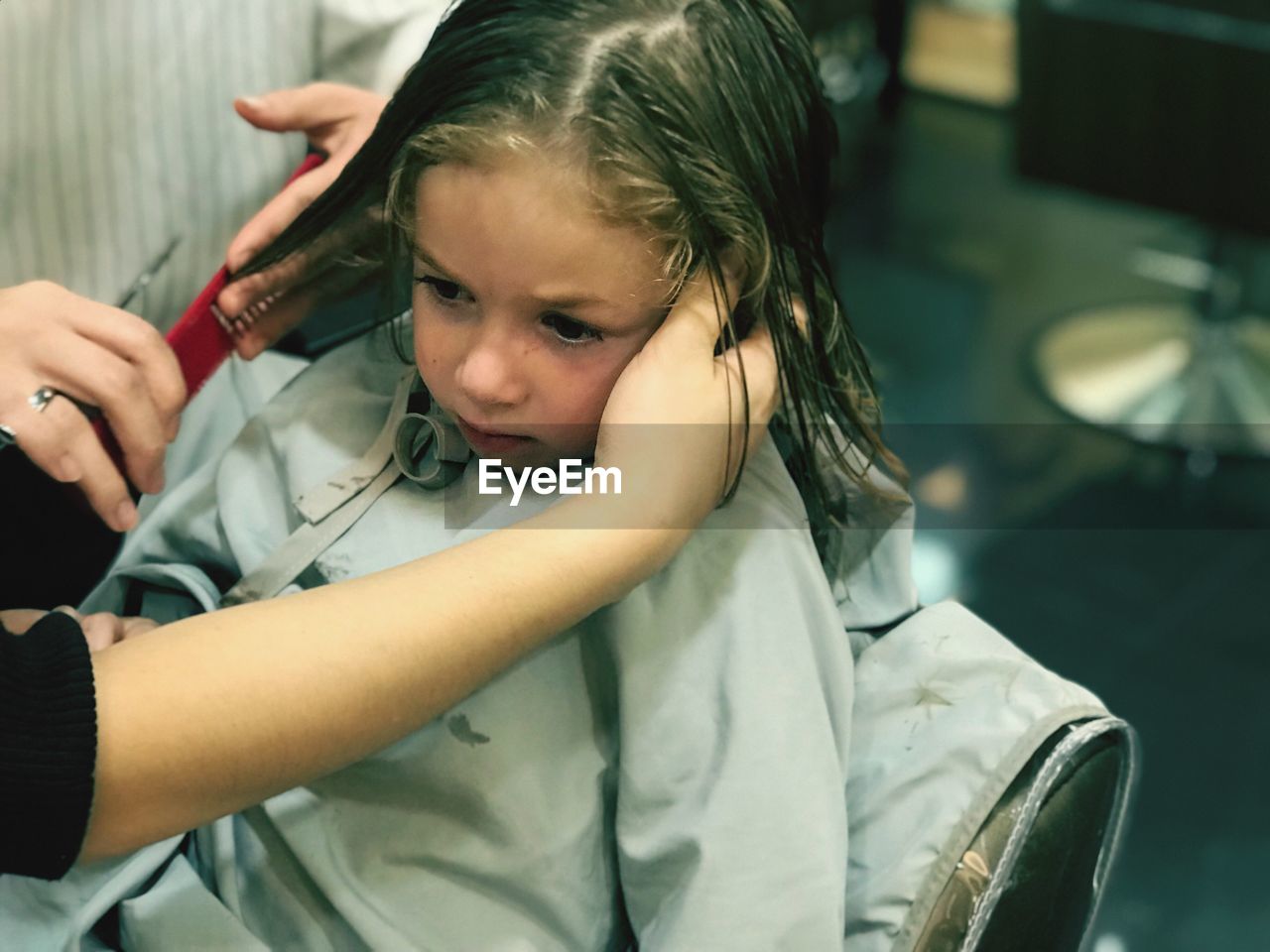 Cropped hand of hairdresser cutting girl hair in shop