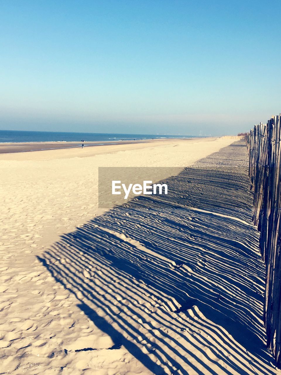 Shadow of fence on beach against sky