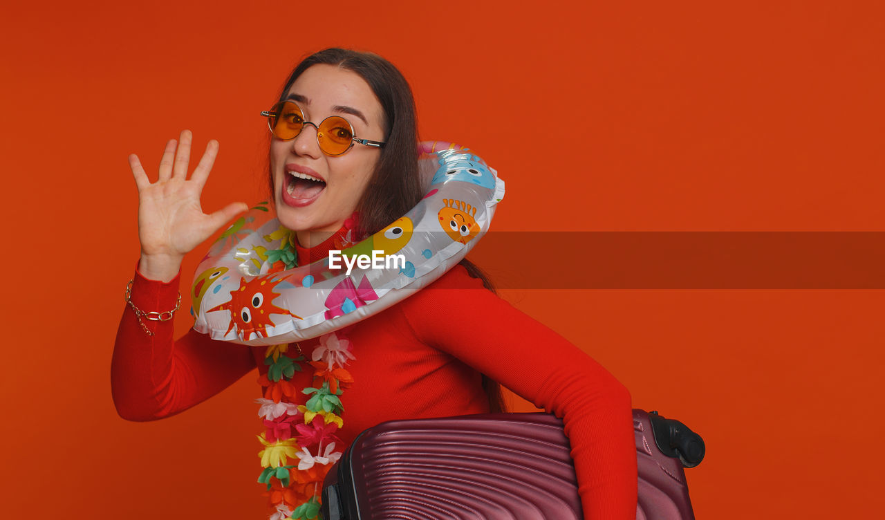 one person, colored background, red, studio shot, adult, women, glasses, happiness, emotion, smiling, fashion, portrait, eyeglasses, indoors, young adult, fun, mouth open, cheerful, clothing, red background, positive emotion, laughing, gesturing, human mouth, person, waist up, looking at camera, facial expression, female, arts culture and entertainment, front view, copy space, arm, enjoyment, humor, shouting, celebration, human limb, limb, event