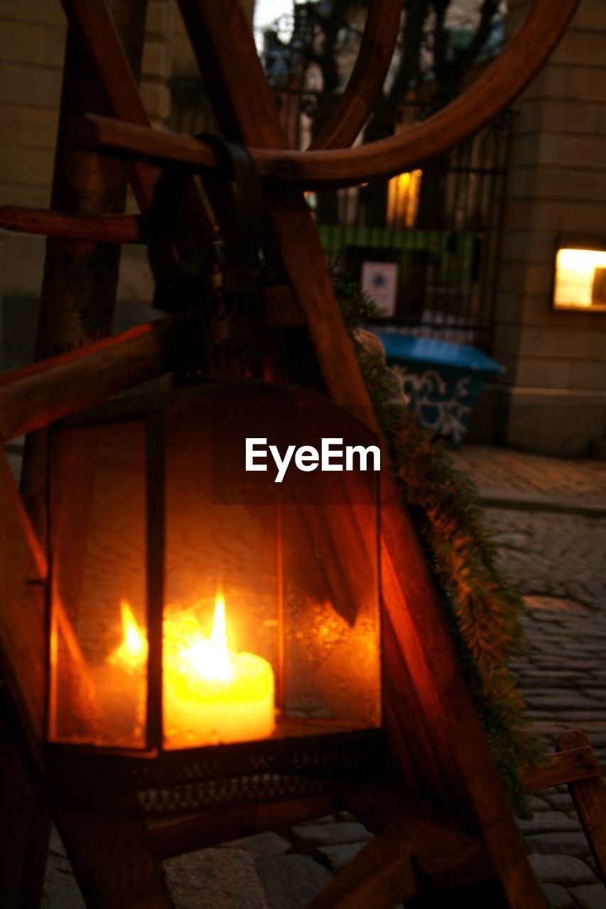 Lantern with melting candle hanging on wooden outdoor structure