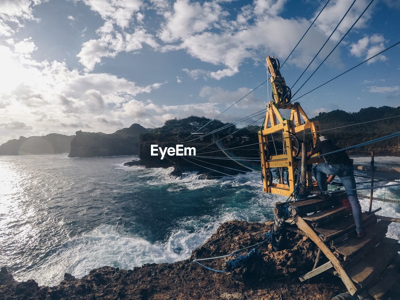 Man standing by overhead cable car over sea against sky