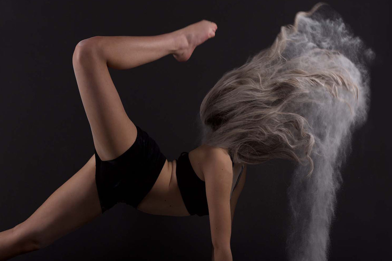 Side view of young woman dancing with flour against wall