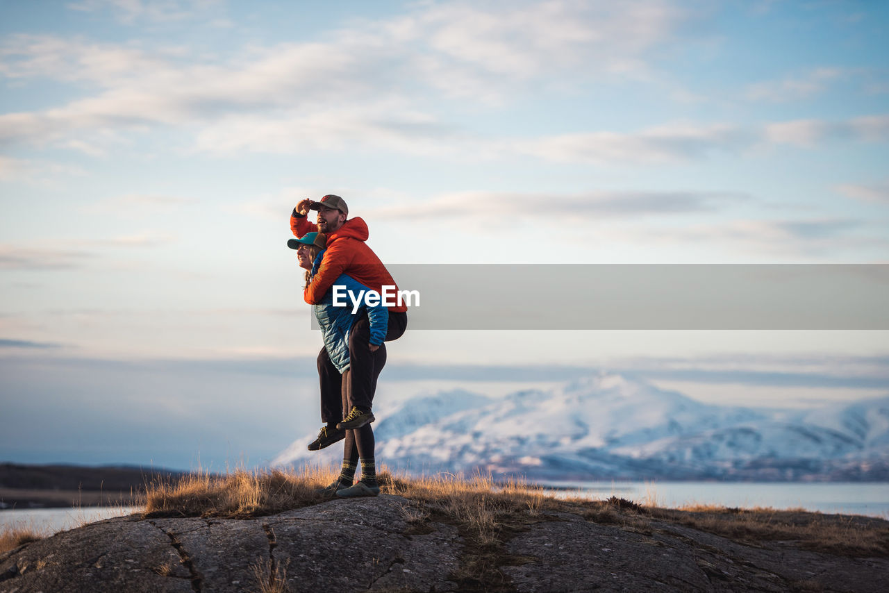 Woman giving man piggyback with mountains behind them