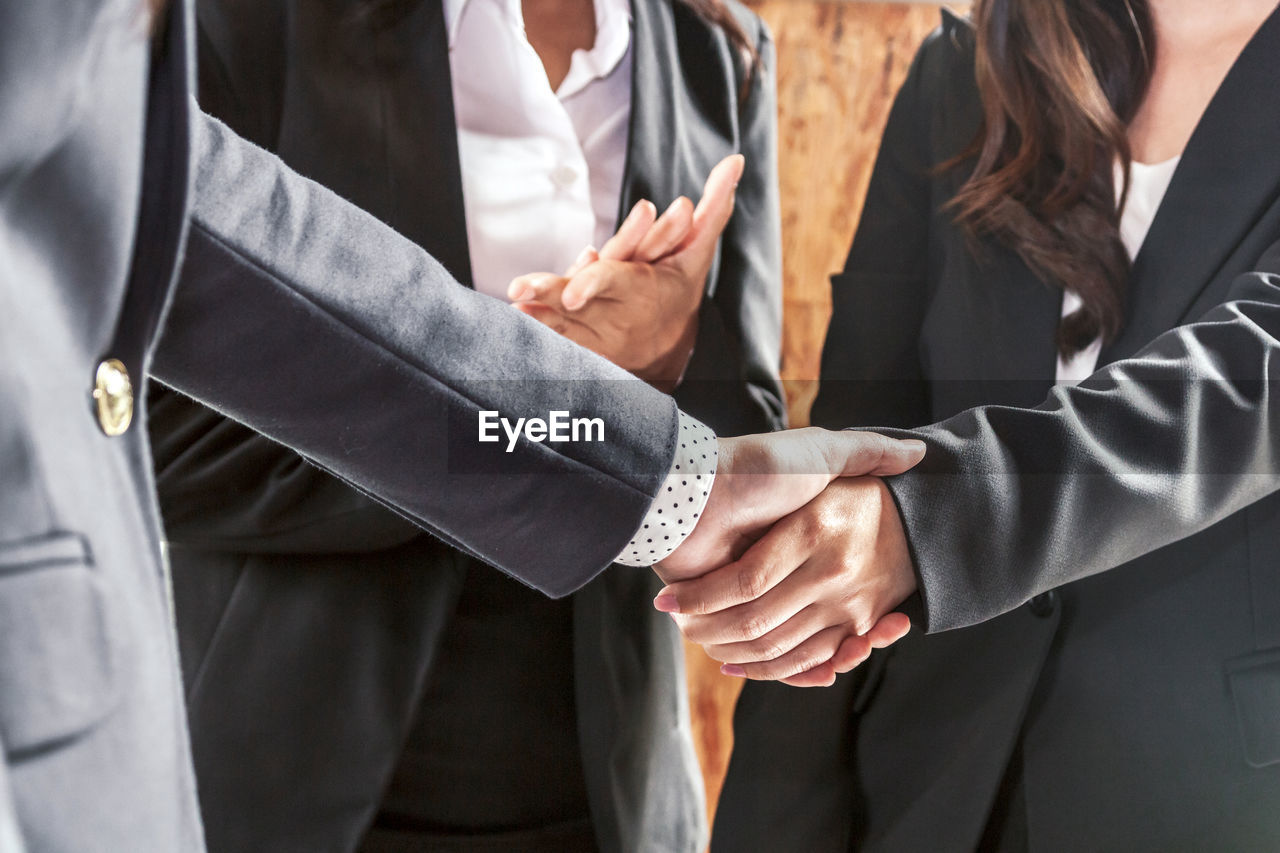 Midsection of woman clapping by colleagues handshaking in office