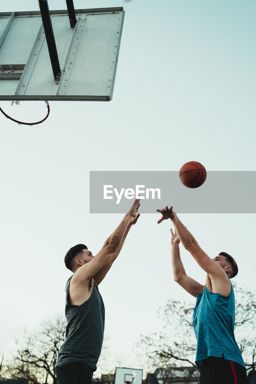 Low angle view of men playing basketball against clear sky