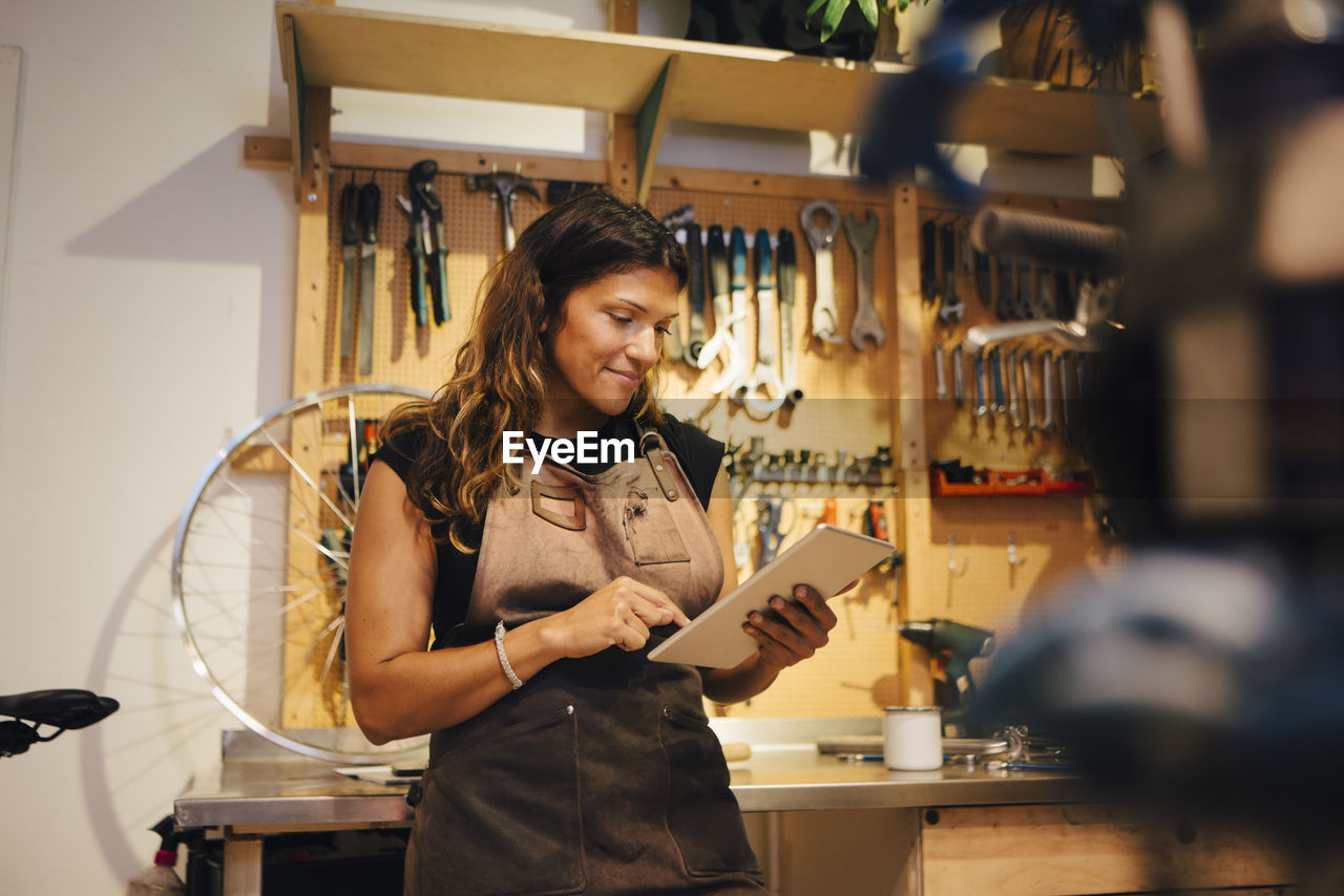 Smiling female owner using digital tablet at bicycle workshop