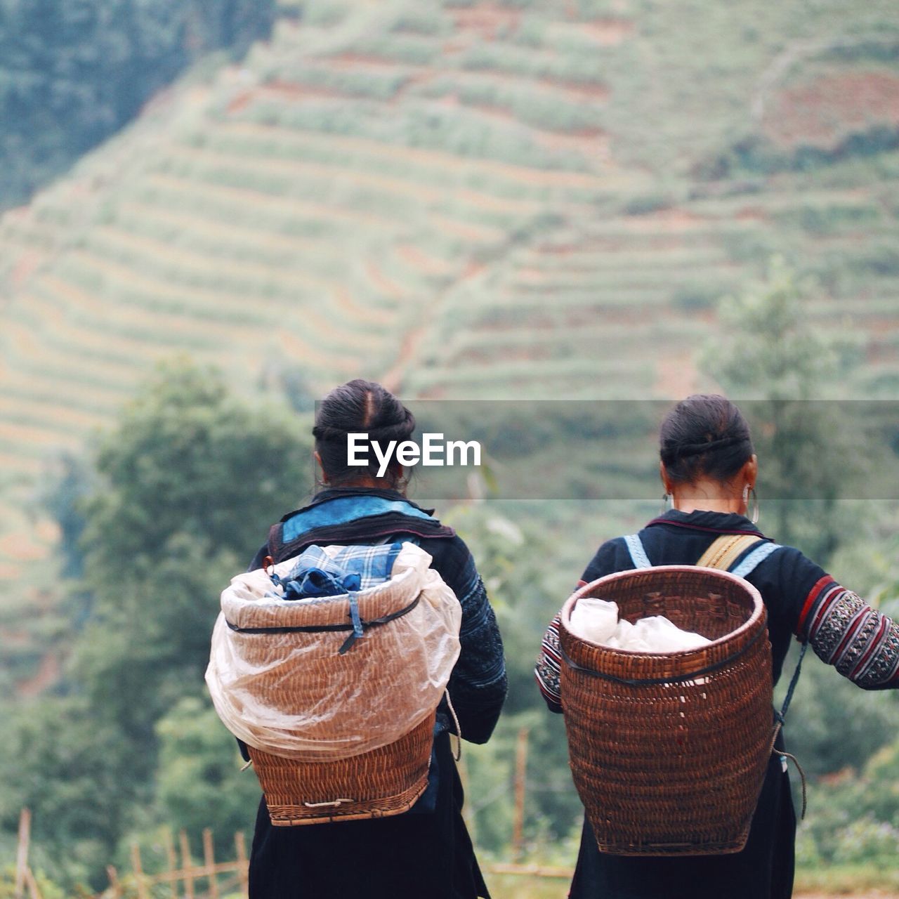 Rear view of women with wicker baskets on field by mountain