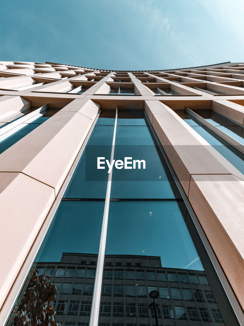 View looking up at the blue sky against tall building with teal windows with perspective