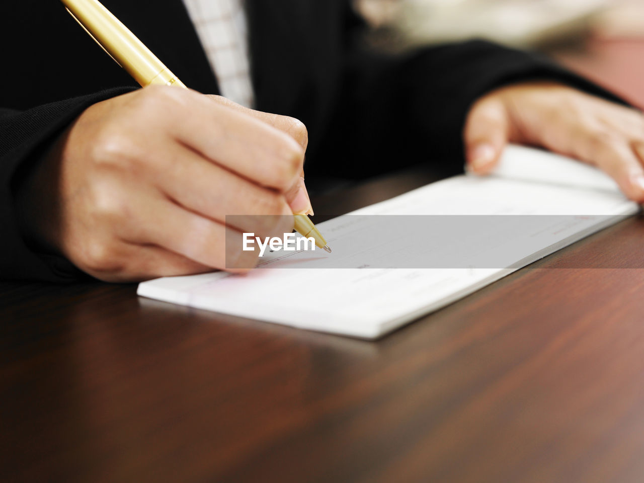 Close-up of midsection person filling cheque book on desk