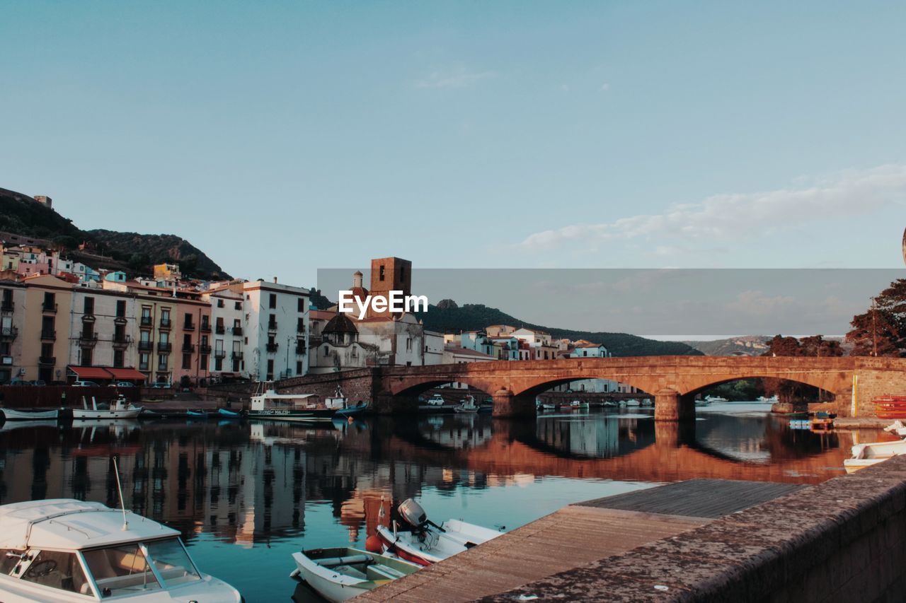 Bridge over river by buildings in city against sky