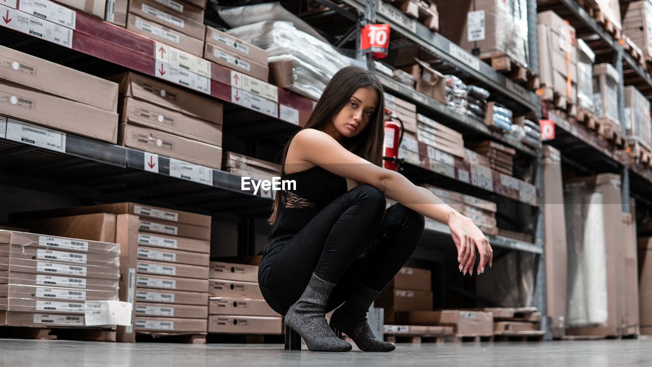Full length portrait of young woman crouching on floor in warehouse