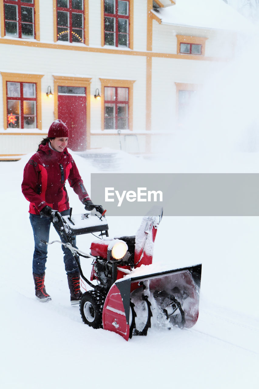 Woman using snowblower in front of house