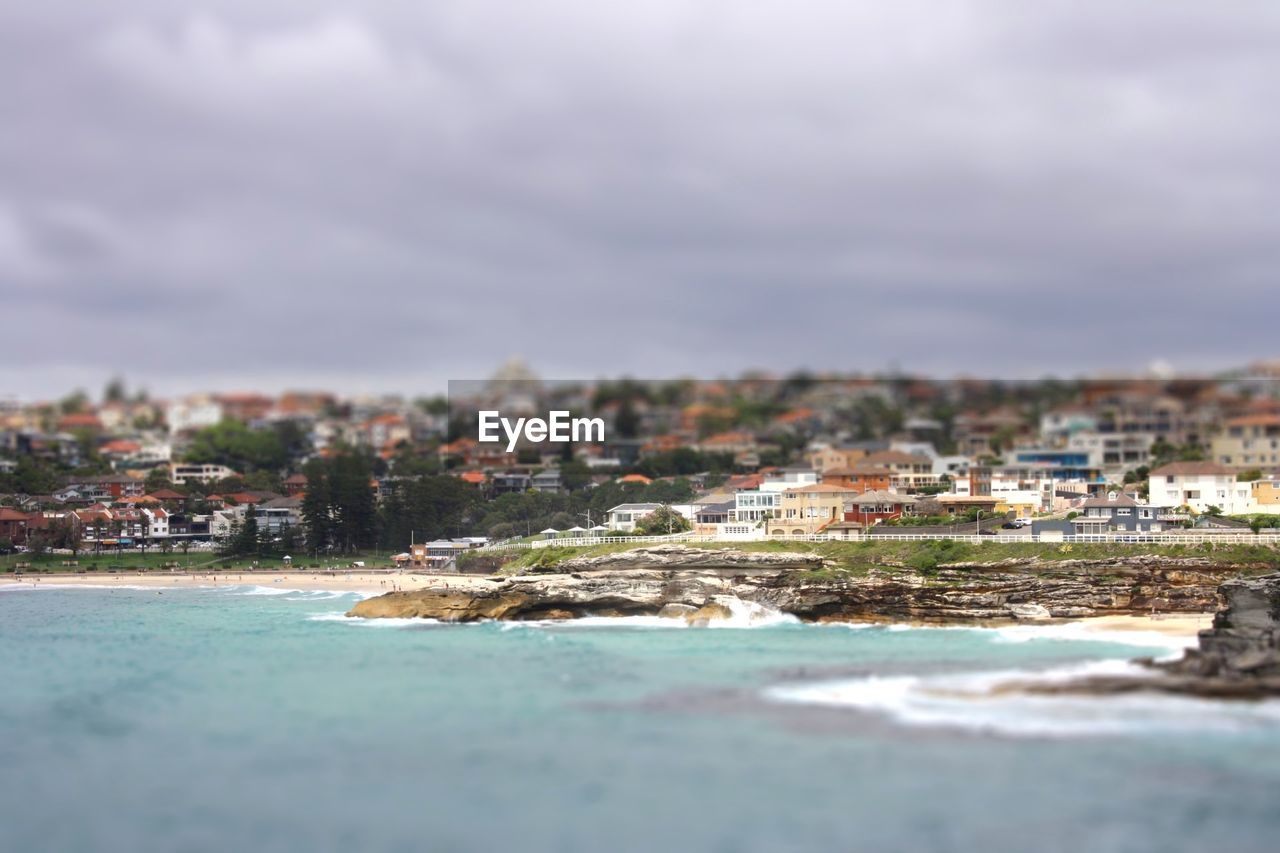 Scenic view of sea by cityscape against cloudy sky