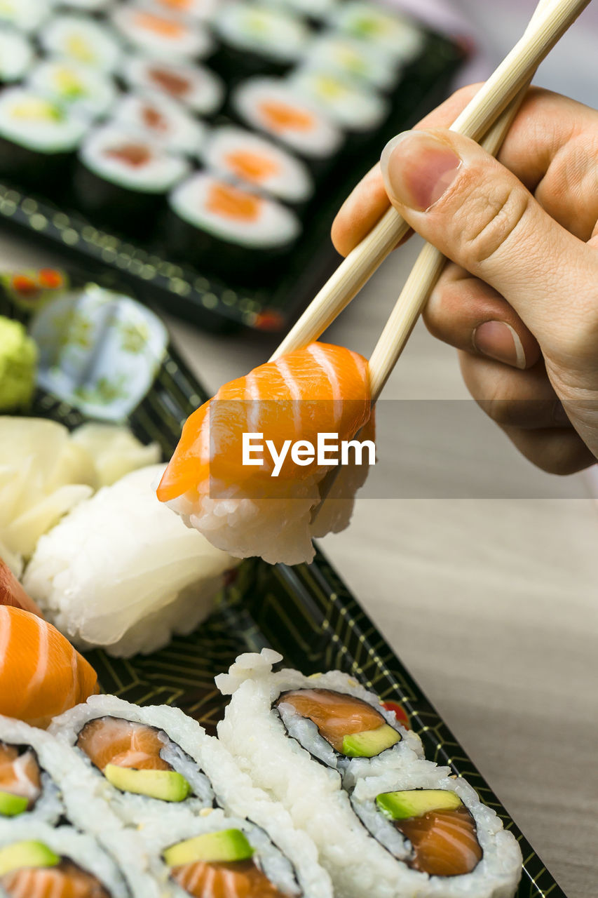 Cropped hand having sushi and sashimi in box on table