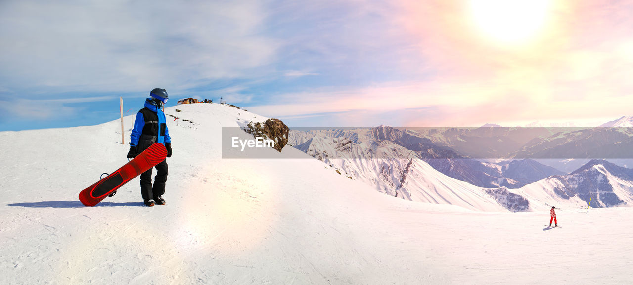 Snowboarder holding snowboard standing on top of mountain