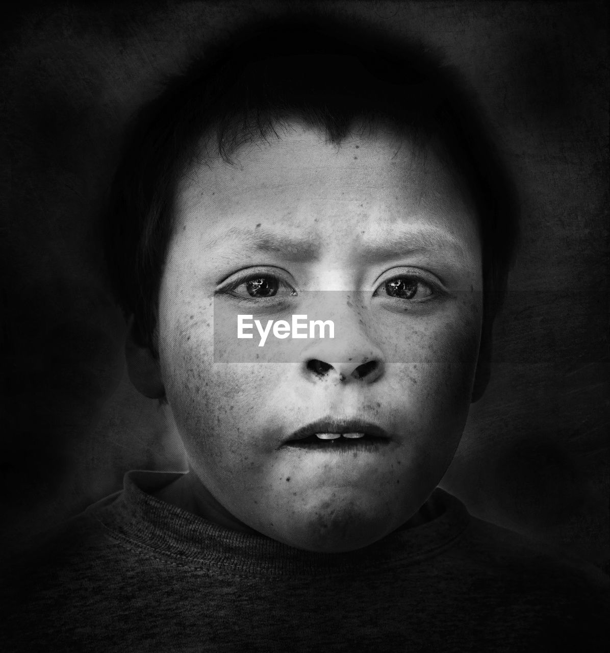 Close-up portrait of boy with freckles on face against black background