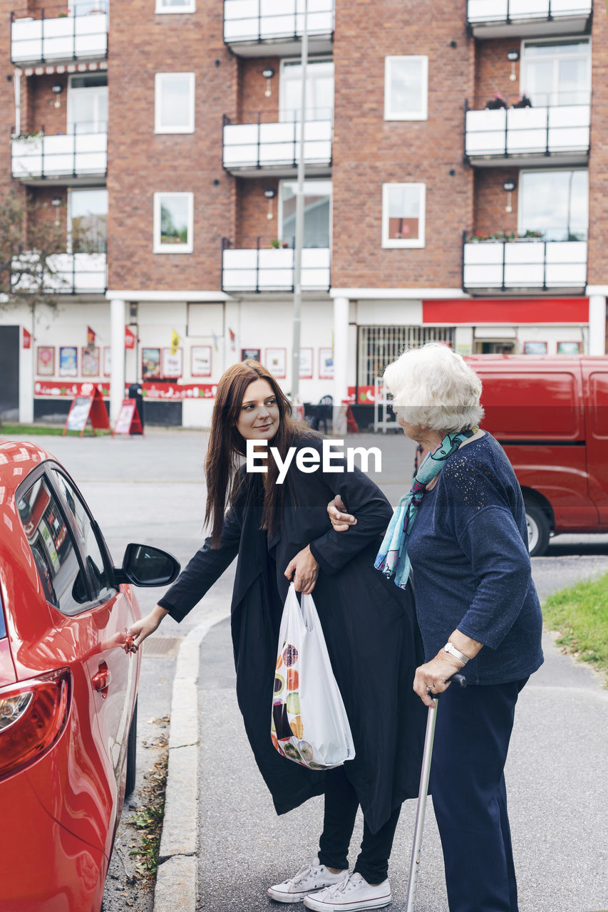 Young woman opening car door for grandmother on city street