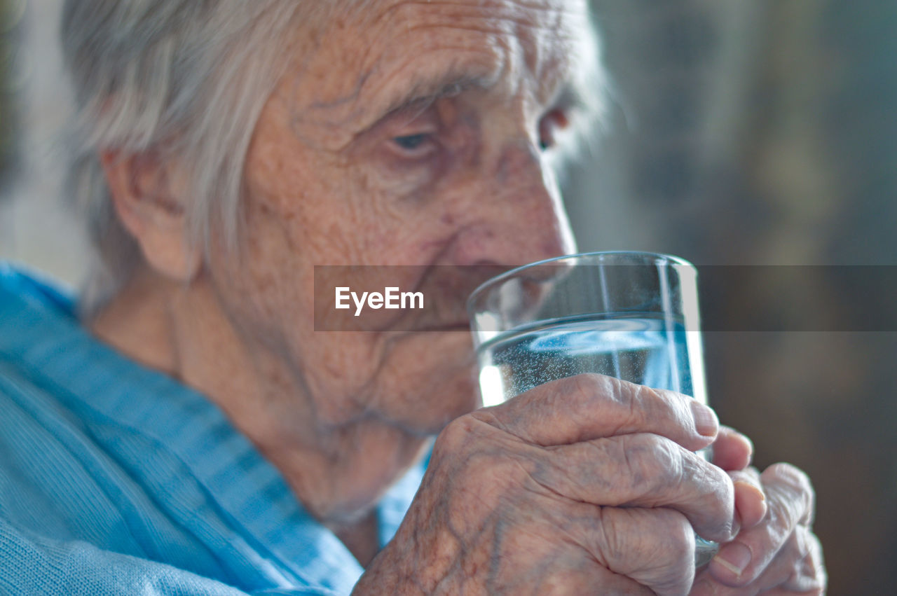 An elderly 90-year-old gray-haired woman who drinks water from a glass. loneliness, stress