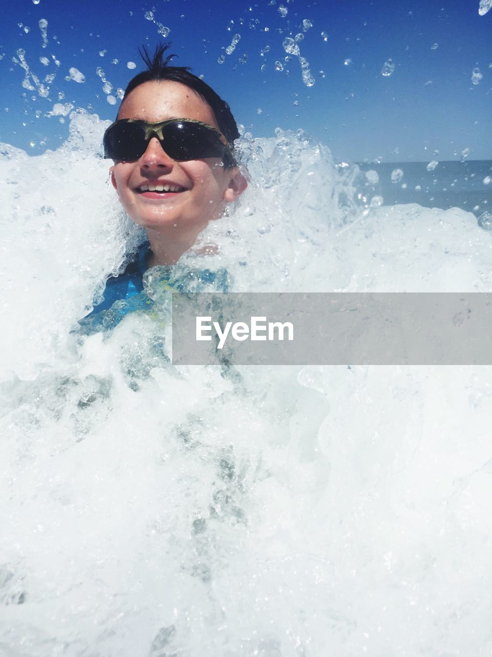 Cheerful boy wearing sunglasses enjoying in sea waves