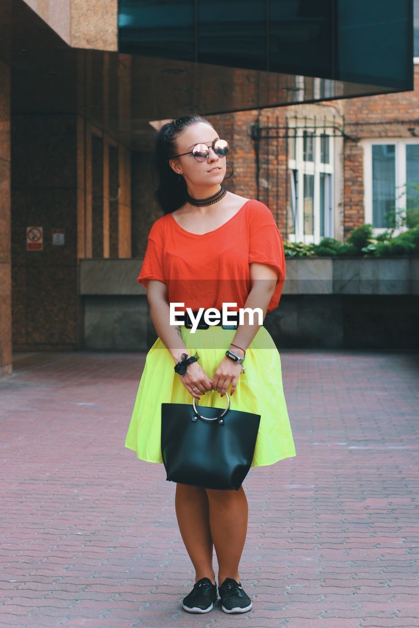 Full length of young woman holding purse while standing on walkway