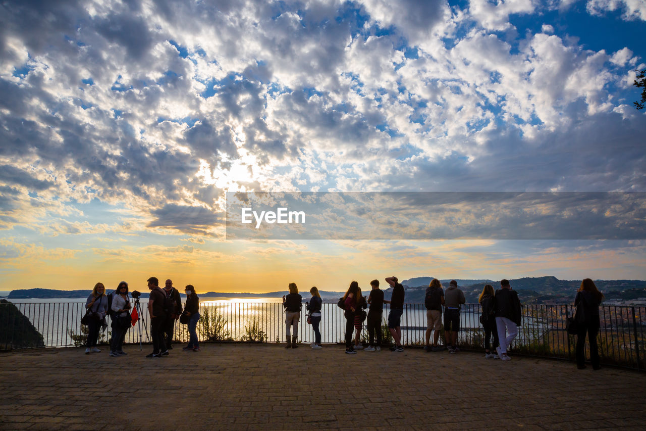 GROUP OF PEOPLE ON BEACH AGAINST SKY DURING SUNSET