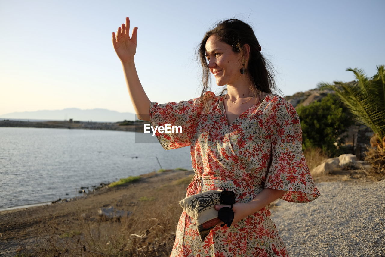 Woman with arms raised standing on shore against sky