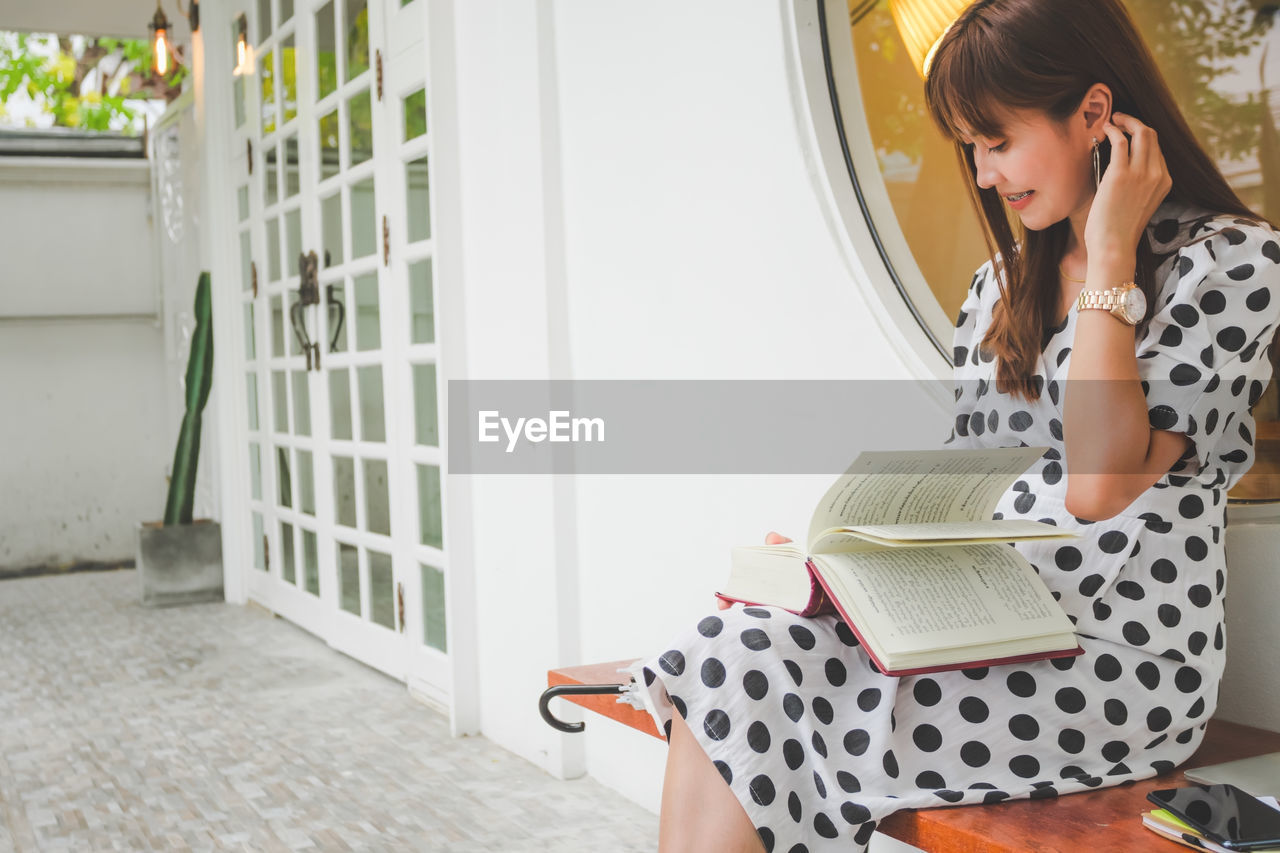 Young woman reading book while sitting on bench