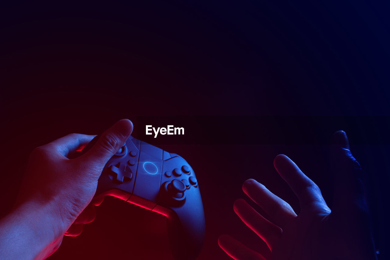 Close-up of hand holding game controller against black background