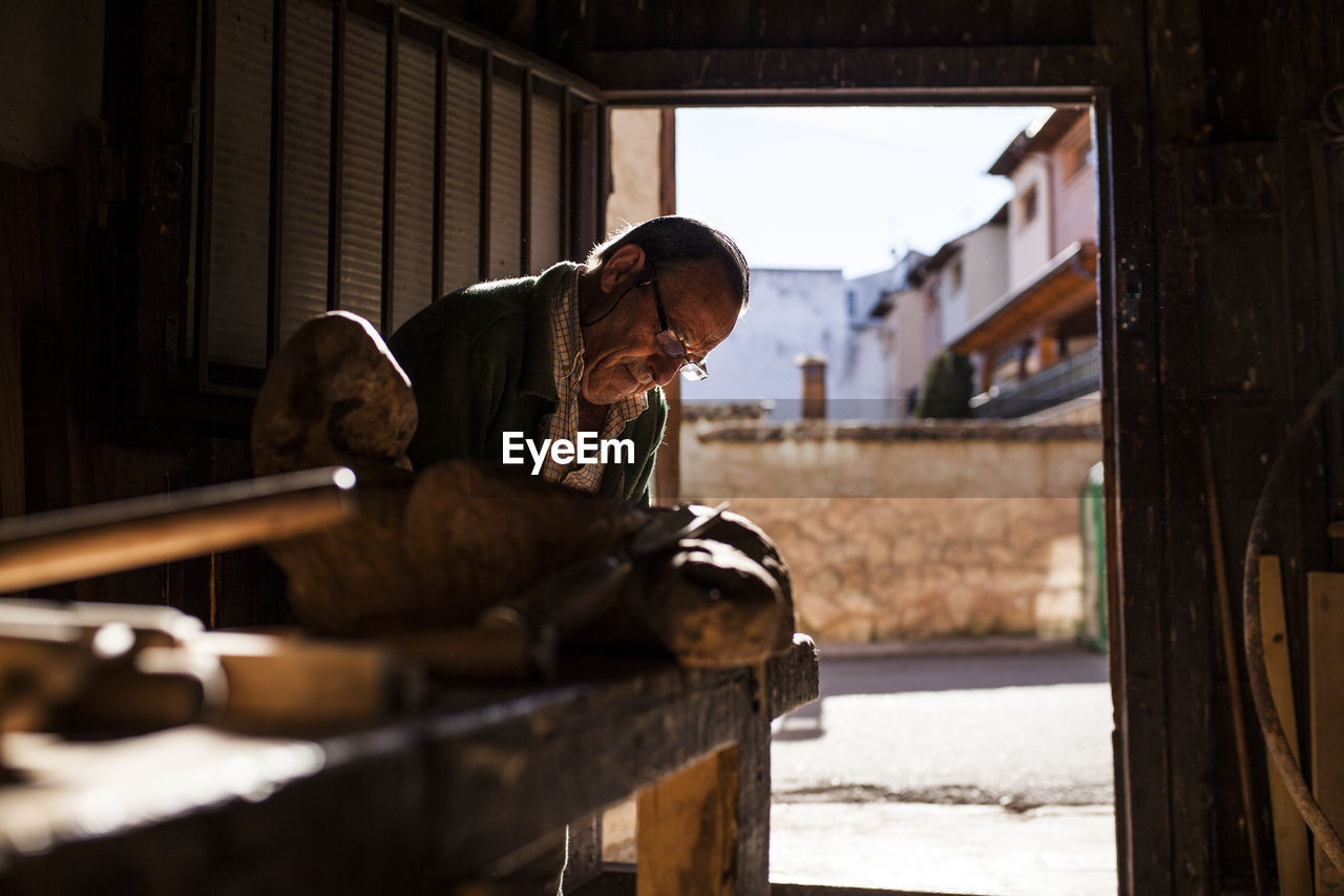 Senior woodworker in glasses working with piece of lumber in workshop