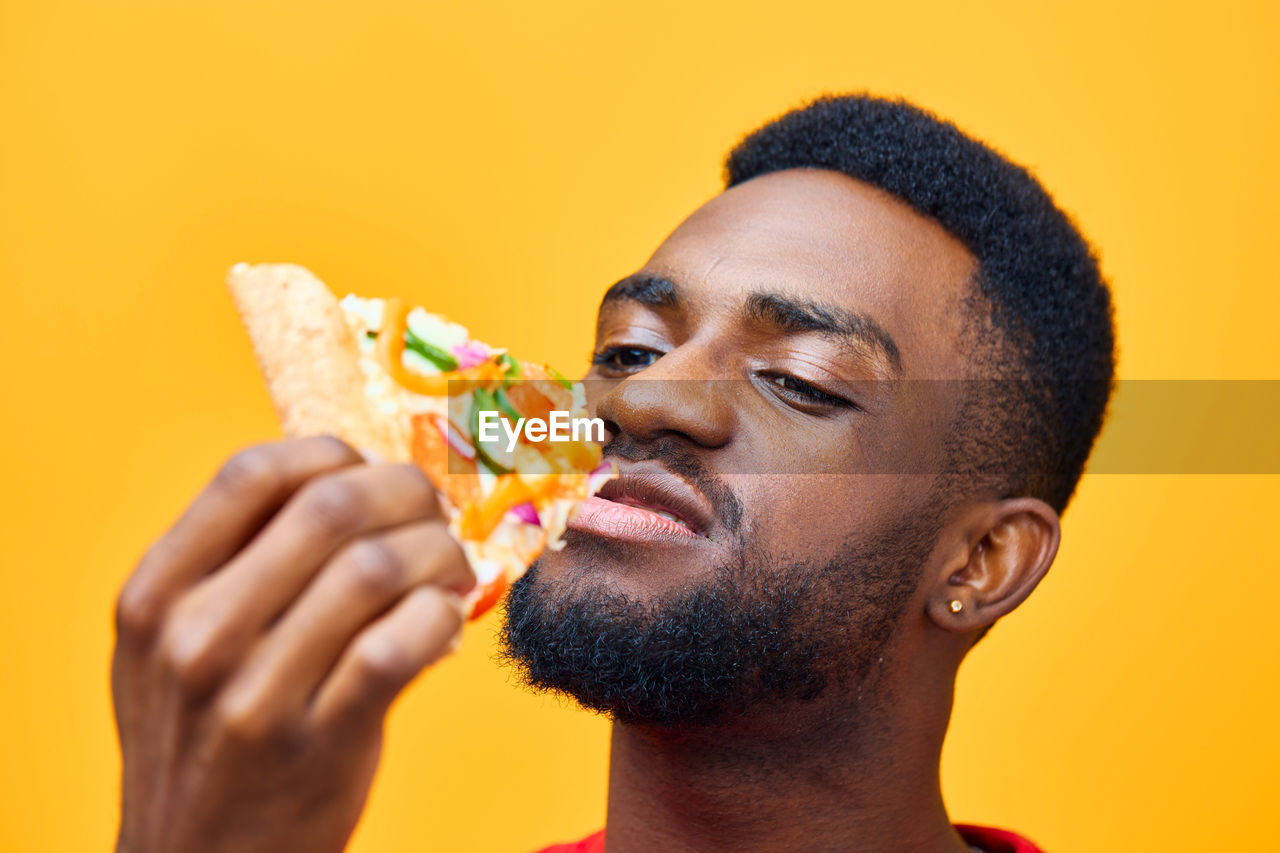 side view of young man eating food against yellow background