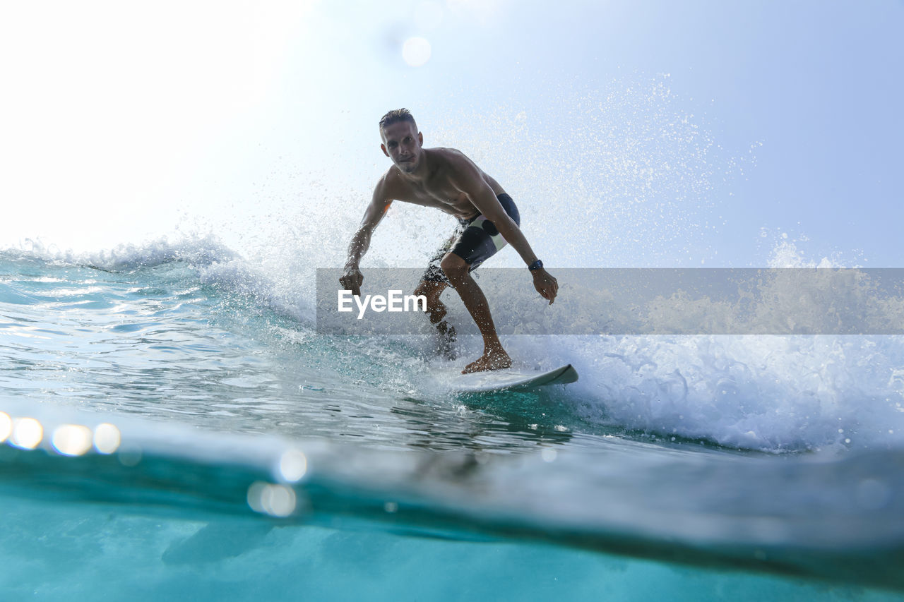 Man with surfboard surfing on sea wave against clear sky