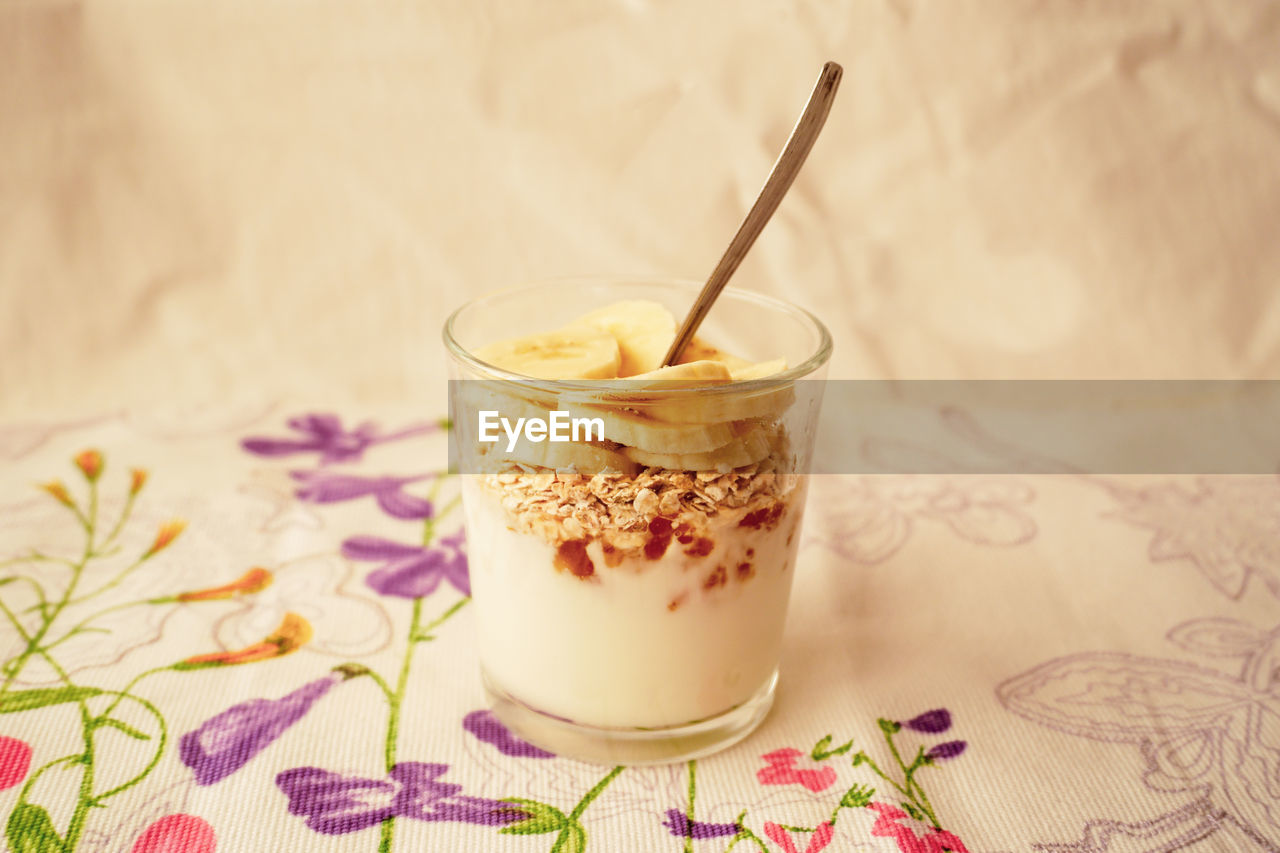Close-up of a glass of yogurt, jam, oat flakes and banana on a table