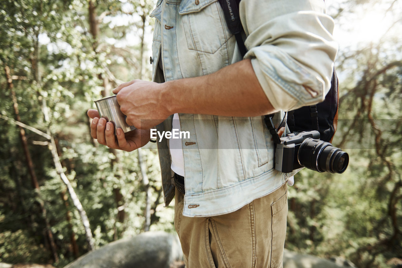 Midsection of man having drink while standing in forest