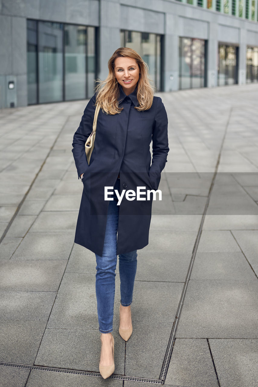 Portrait of smiling mature woman walking street against building