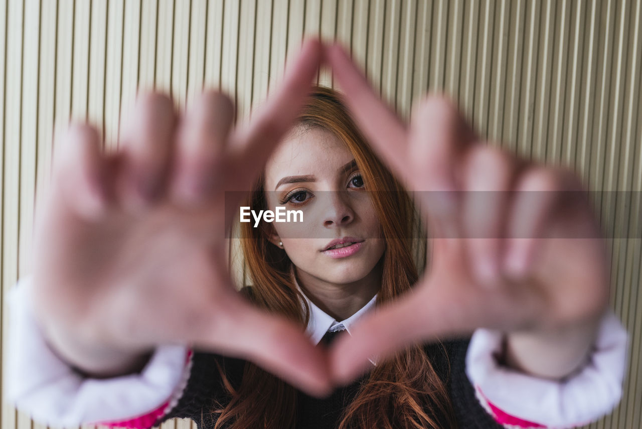 Serene female in stylish clothes looking at the camera and making shapes with his hands