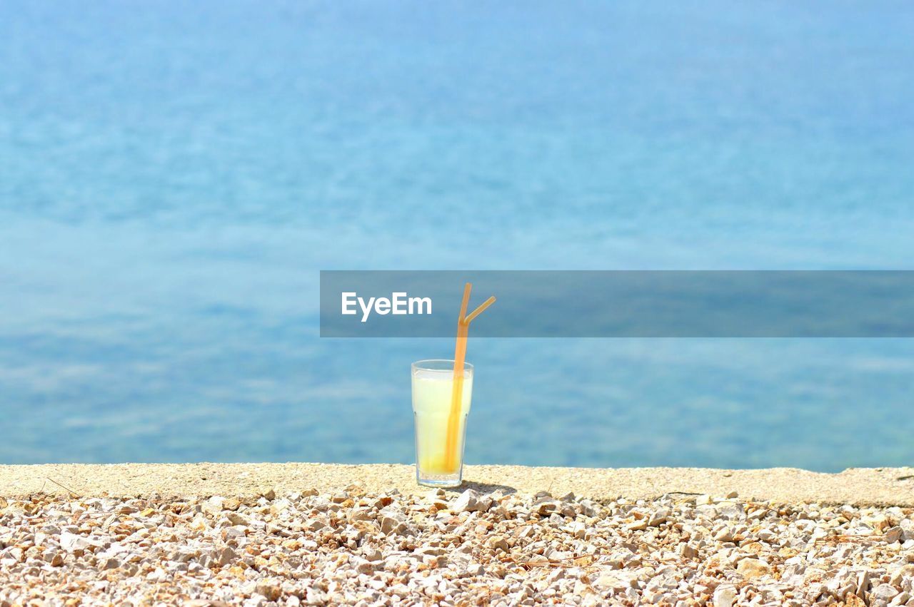 Glass of drink with straw at beach