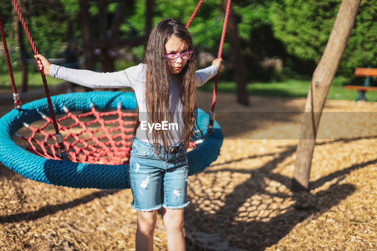 Portrait of a beautiful caucasian dissatisfied girl with a round rope swing in the park