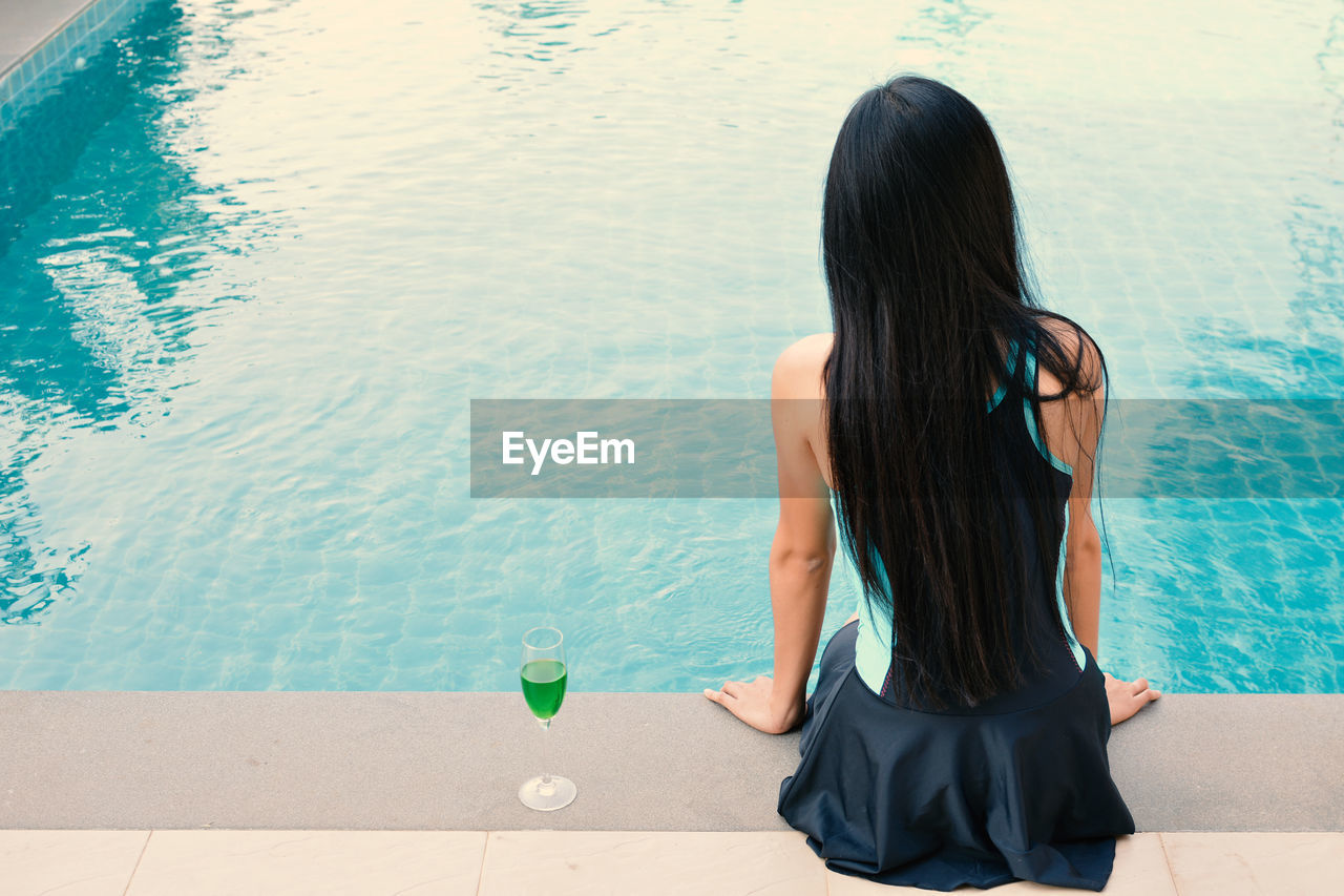 Rear view of woman sitting at poolside