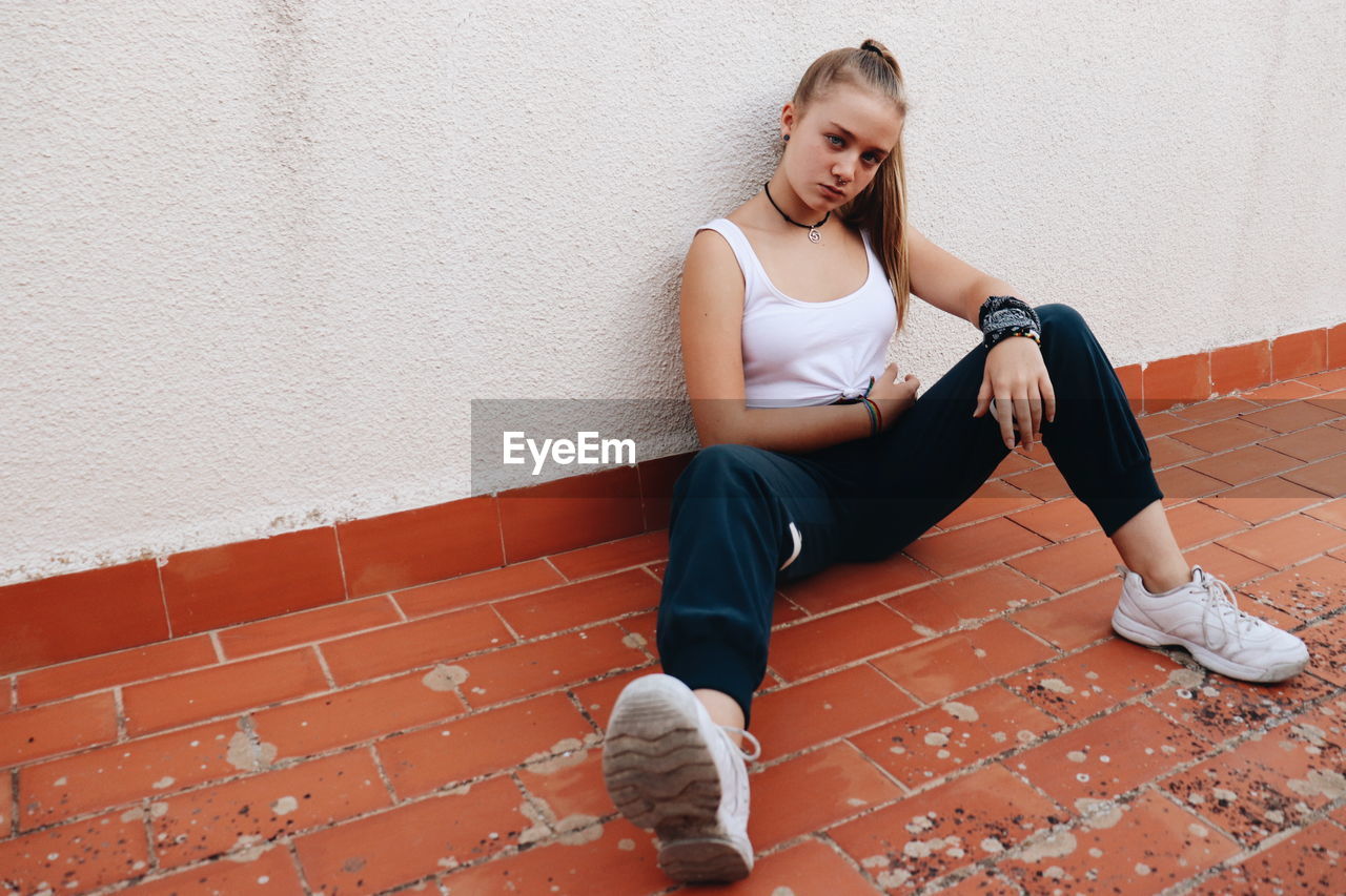 Full length of woman sitting against wall