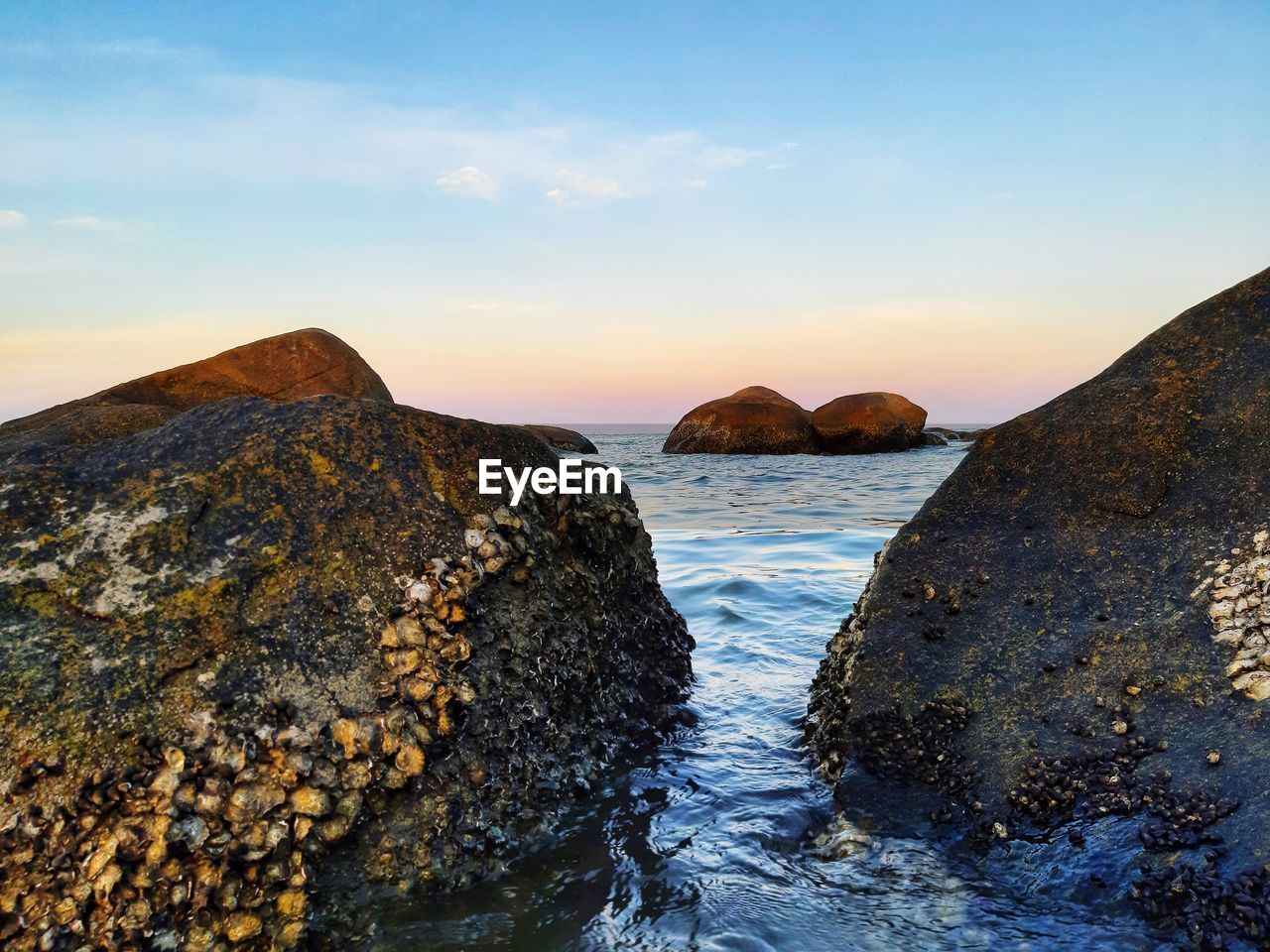 Rocks in sea against sky during sunset