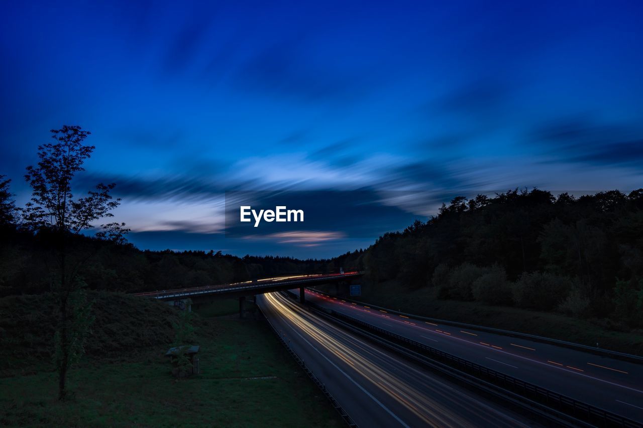 LIGHT TRAILS ON ROAD AGAINST BLUE SKY