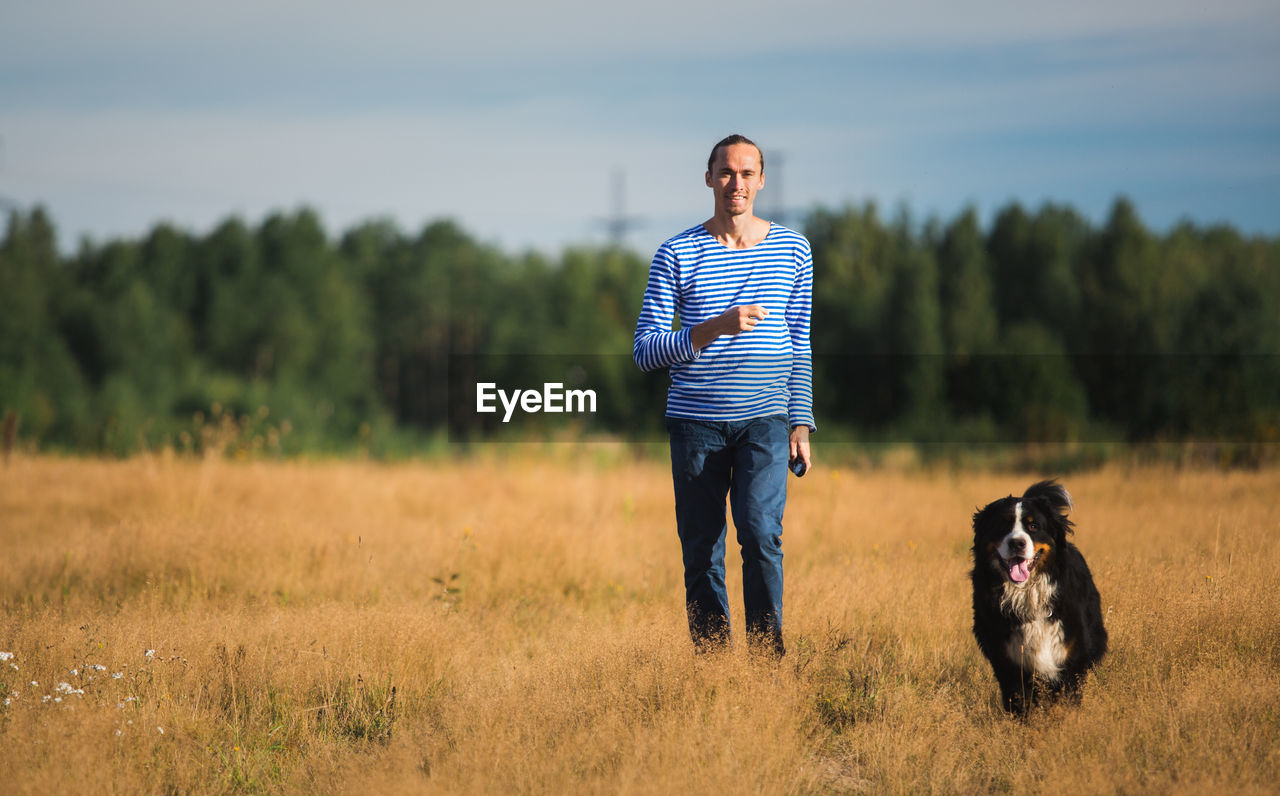 Portrait of man with dog standing on grassy land