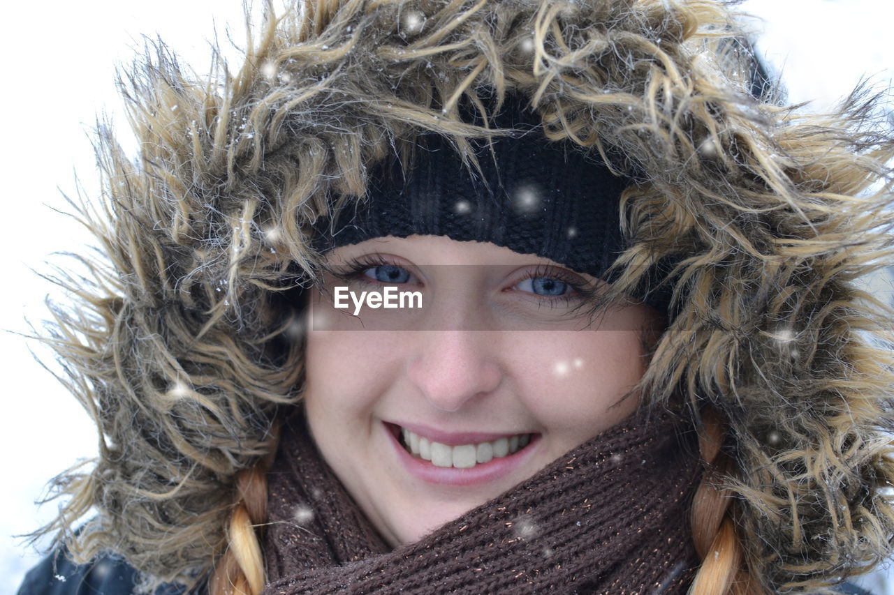 Close-up portrait of smiling young woman during snowfall