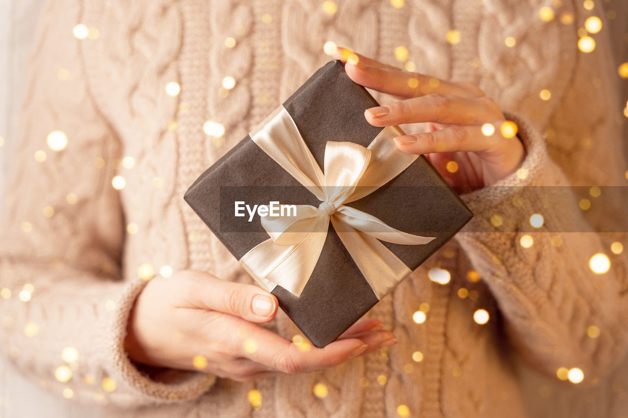 A box with a gift wrapped in brown paper and tied with a gold ribbon, in female hands, close-up