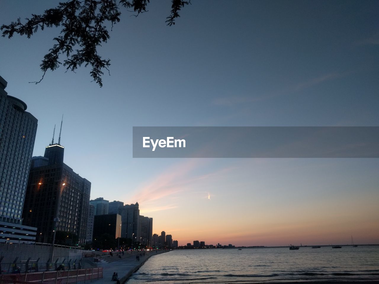 City buildings by sea against sky at sunset