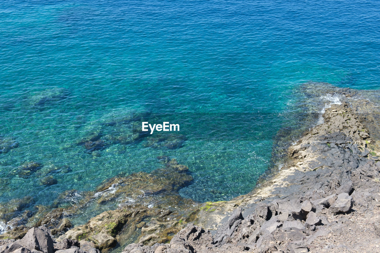 water, sea, beauty in nature, scenics - nature, land, high angle view, blue, nature, day, tranquility, no people, tranquil scene, rock, beach, idyllic, reef, outdoors, coast, ocean, shore, sunlight, turquoise colored, non-urban scene, islet