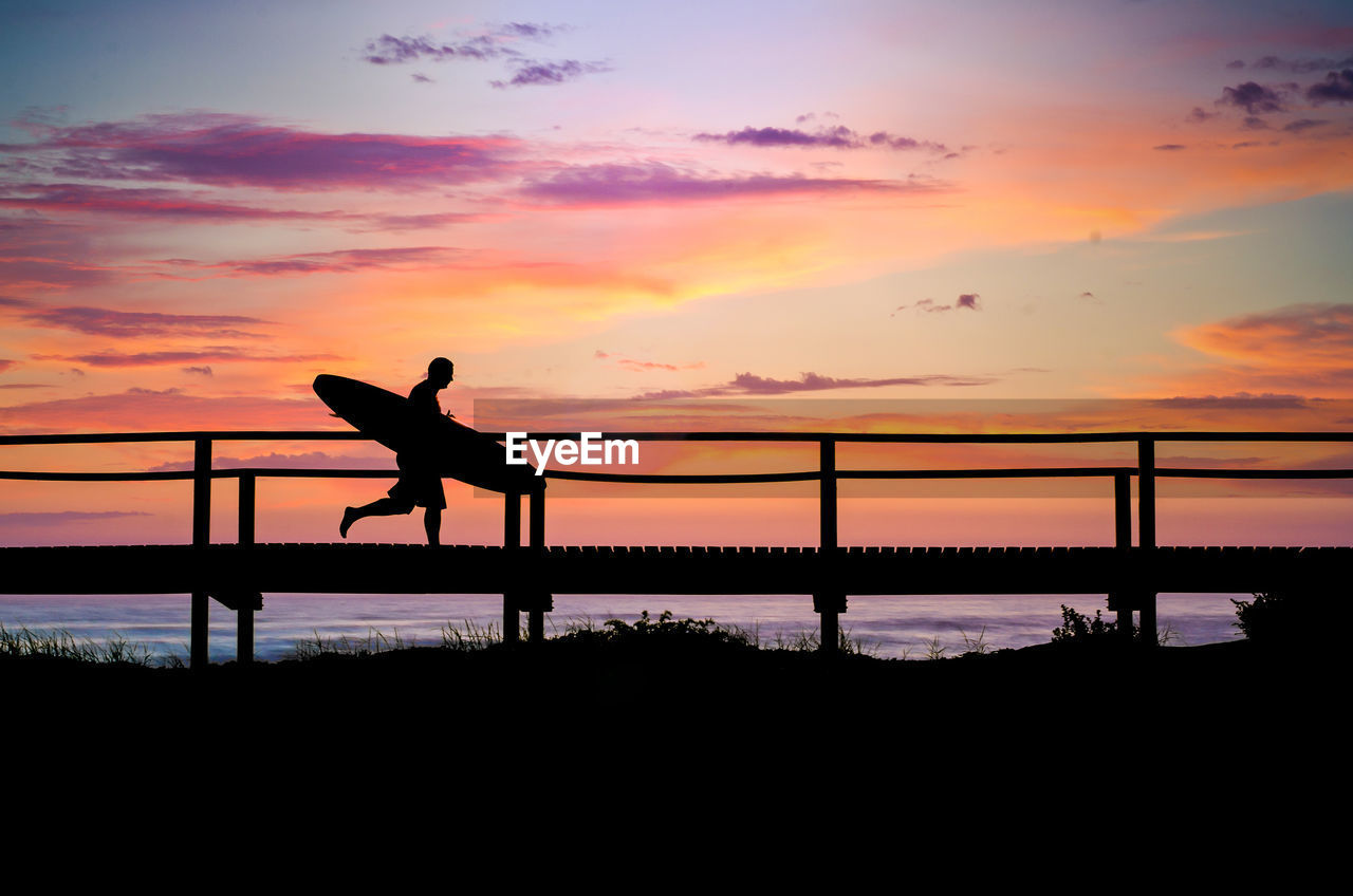 Silhouette man standing by railing against sky during sunset